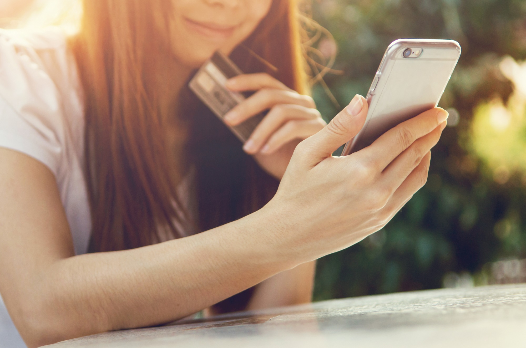 Close-up of a person holding a smartphone in one hand and a credit card in the other, suggesting an online or mobile purchase