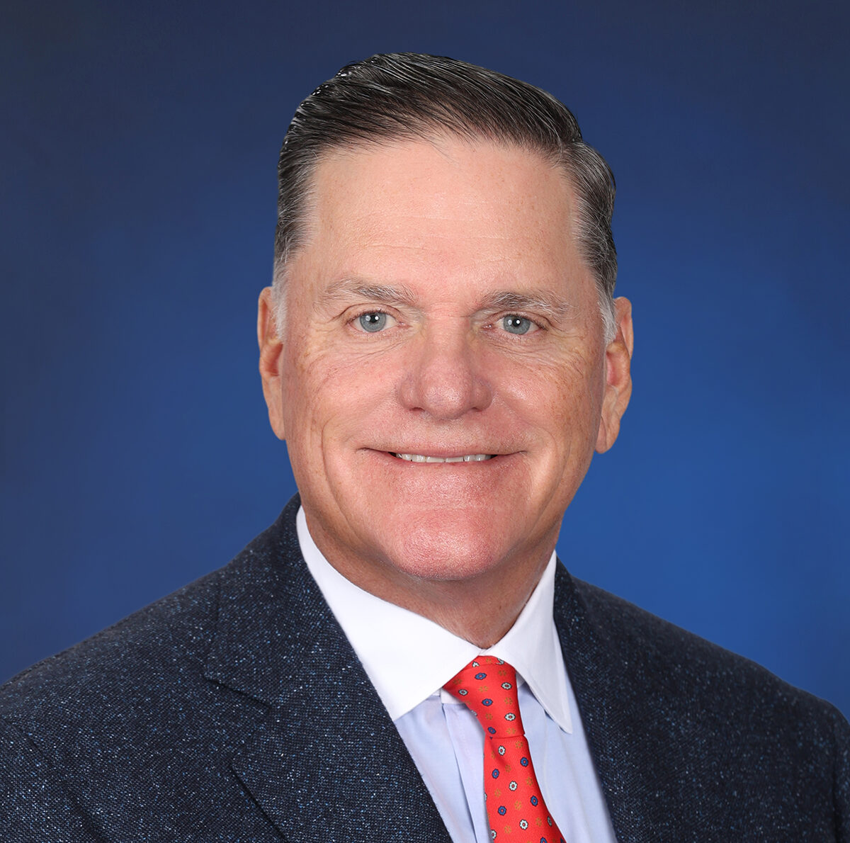 Portrait photo of Brian Parker, Director, shown against a blue background, wearing a suit and tie.